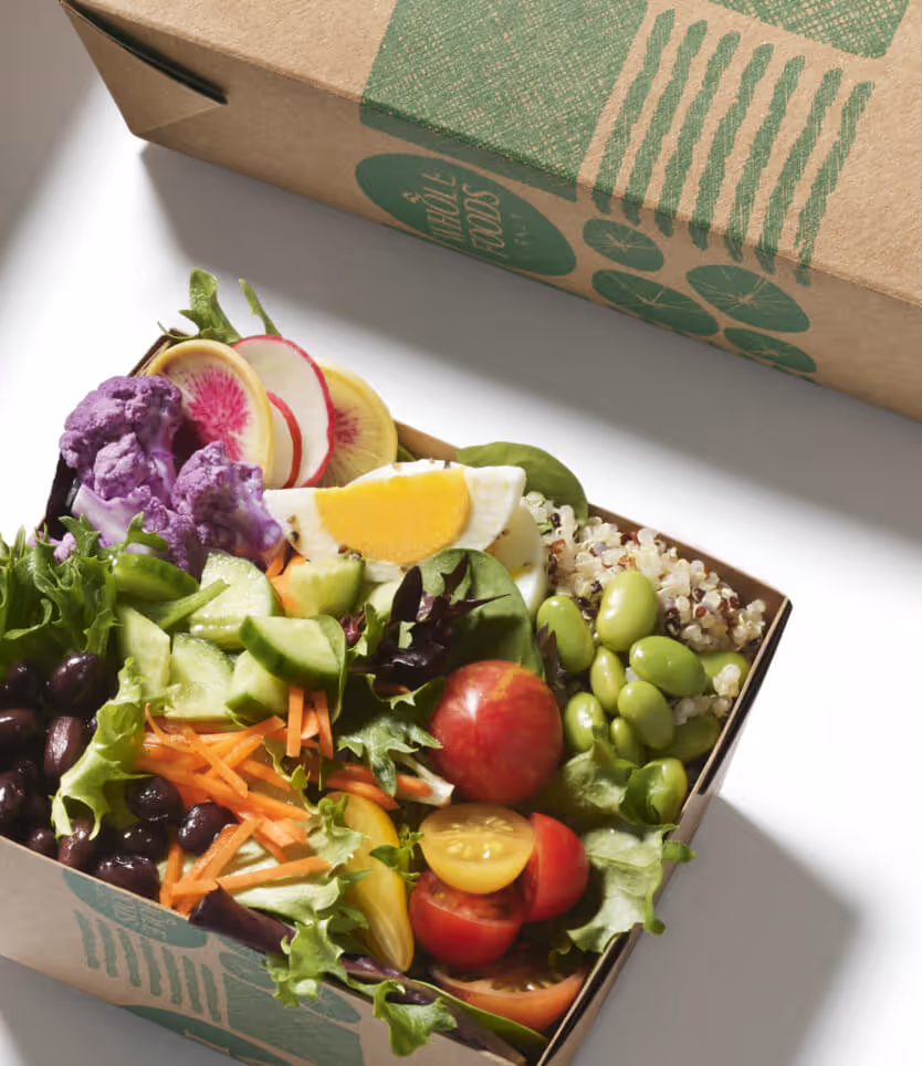 Open box with fresh salad including purple cauliflower, hard-boiled egg, tomatoes, quinoa, and mixed greens.