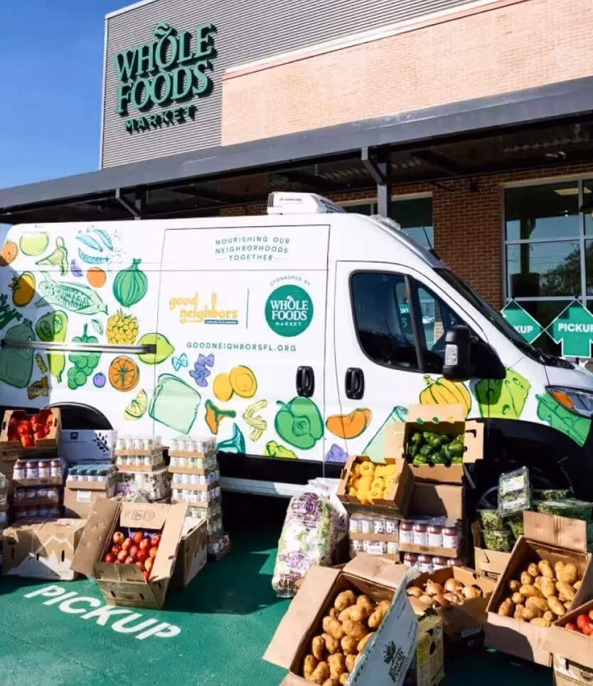 Whole Foods Market pickup area with a delivery van and boxes of fresh produce and groceries outside.