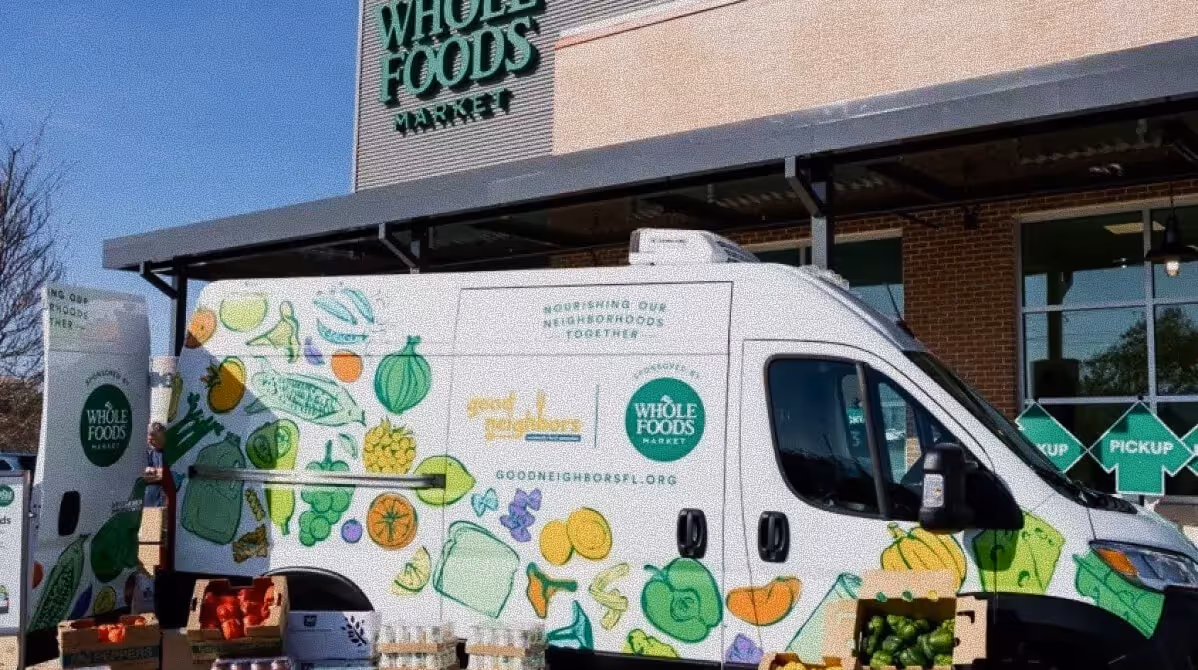 Whole Foods Market delivery van with colorful fruit and vegetable illustrations parked by store for pickup.