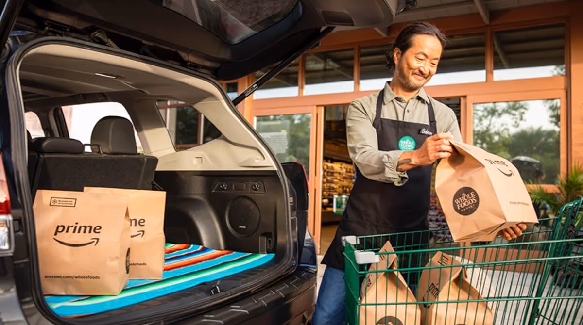Man loading Whole Foods grocery bags from a shopping cart into the back of an SUV.