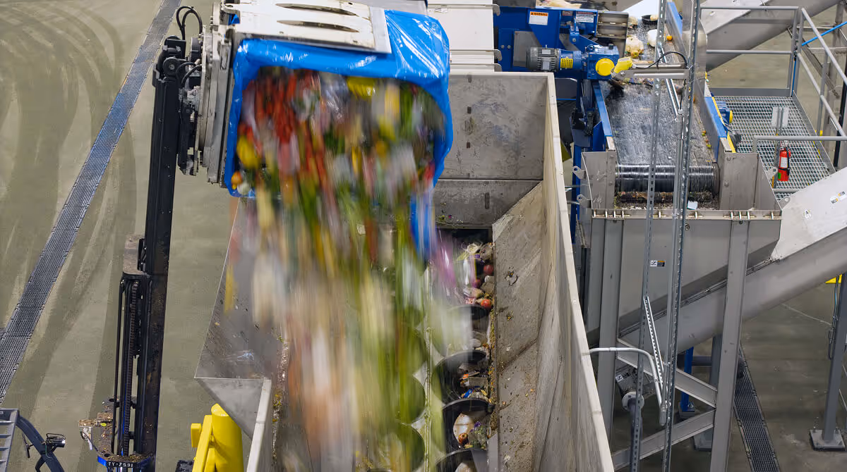 Industrial machine unloading mixed organic waste onto a sorting conveyor belt in a recycling facility.
