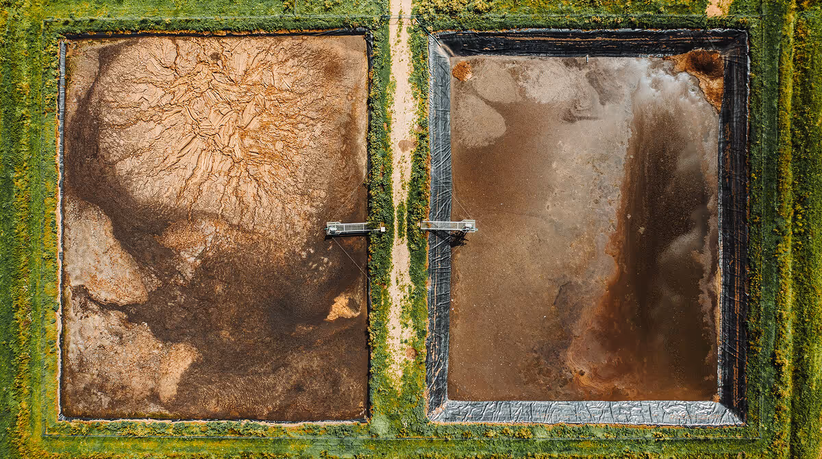 Aerial view of two adjacent rectangular ponds with muddy water, surrounded by grass and a dirt path.